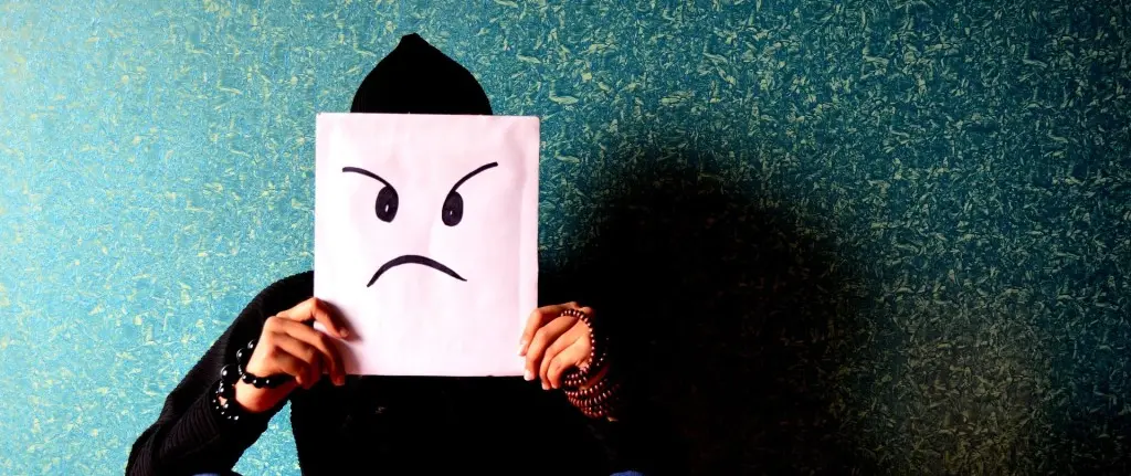 uomo pone davanti la faccia un foglio con l'immagine di una faccia triste stilizzata